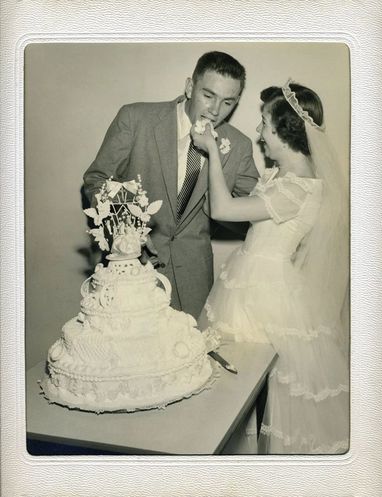 A black-and-white wedding photo of a couple cutting a tiered cake