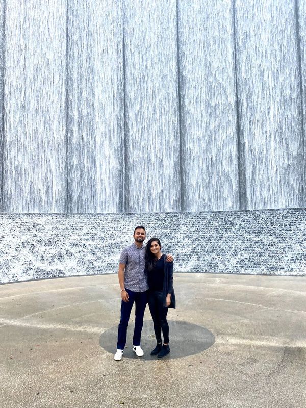 A couple standing arm in arm in front of a towering curved waterfall wall