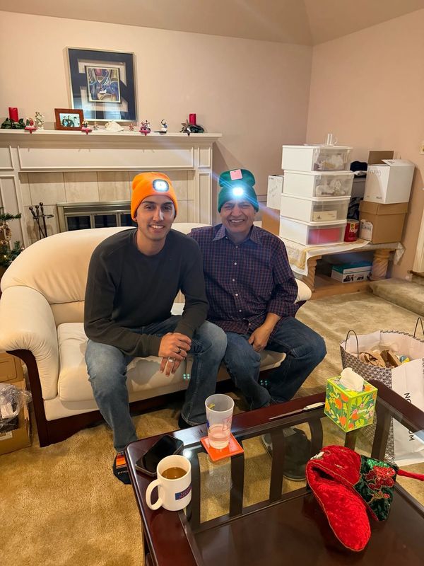 A son and his father on a couch wearing orange and green beanies with glowing headlamps